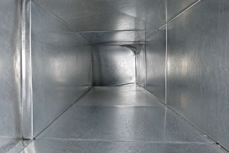 View down the interior of a galvanized metal HVAC supply duct showing smooth clean metal walls and a turn at the far end